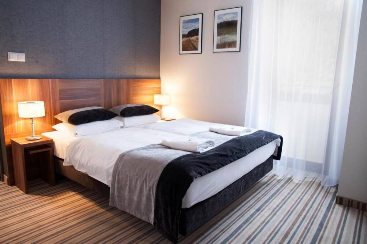 A hotel room with a large bed, two bedside tables with lamps, a striped carpet, and two framed pictures on the wall.