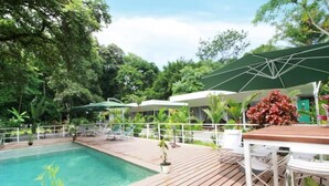 A pool area with a wooden deck, lounge chairs, and umbrellas. - Casa Blanca Villas Ojochal (Ciudad Cortés)