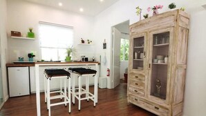 A kitchen with wooden flooring, white bar stools, a white refrigerator, and a vintage cabinet with glass doors. - Casa Blanca Villas Ojochal (Ciudad Cortés)