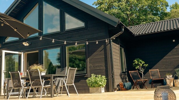 Ein modernes Haus mit Terrasse, Sitzgelegenheiten im Freien und großen Fenstern.