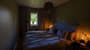 Ein Schlafzimmer mit einem großen Bett, einem Fenster mit Vorhängen, einer Hängelampe und einem Nachttisch mit Lampe.