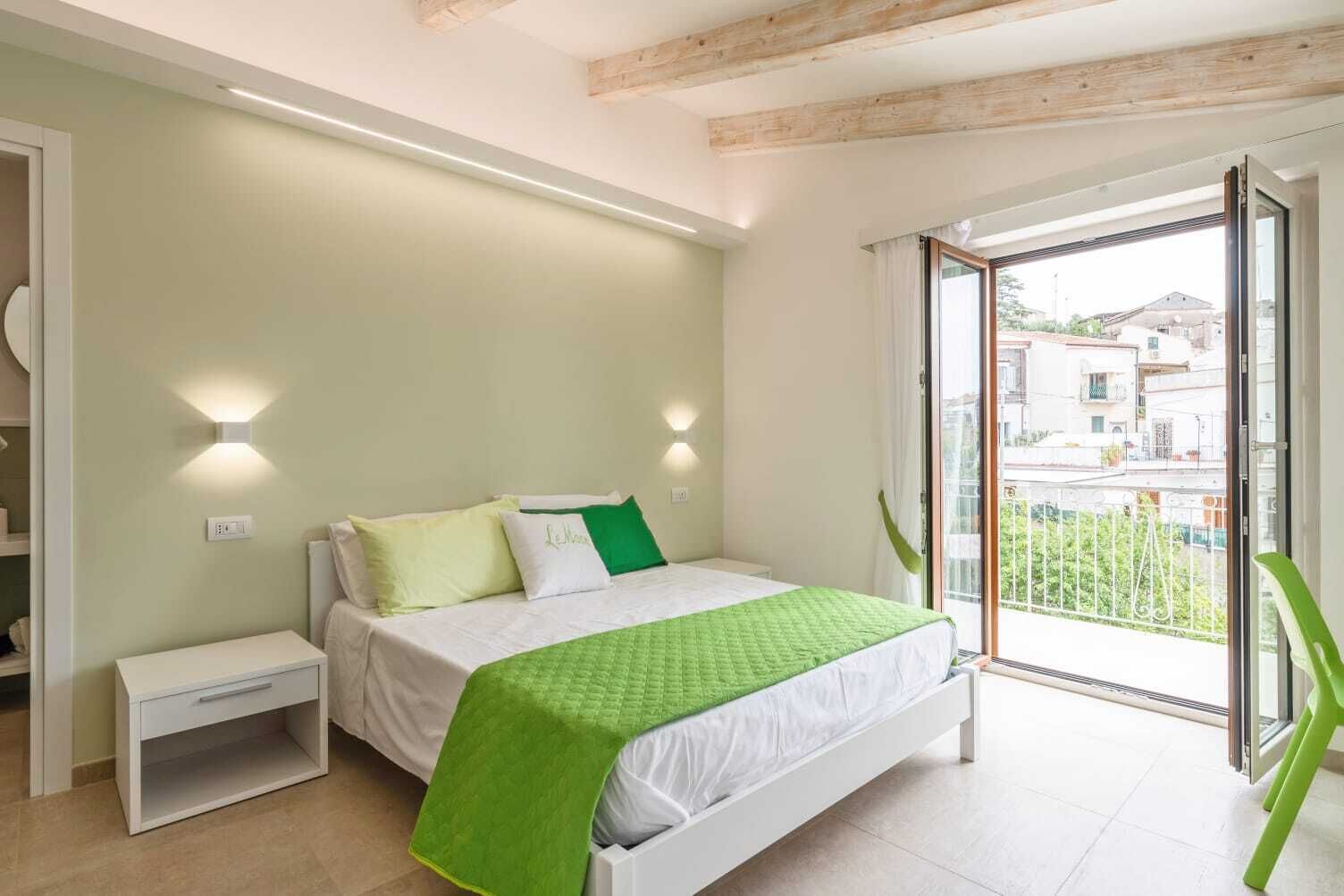 A bedroom with a bed, bedside table, and a view of the outside.