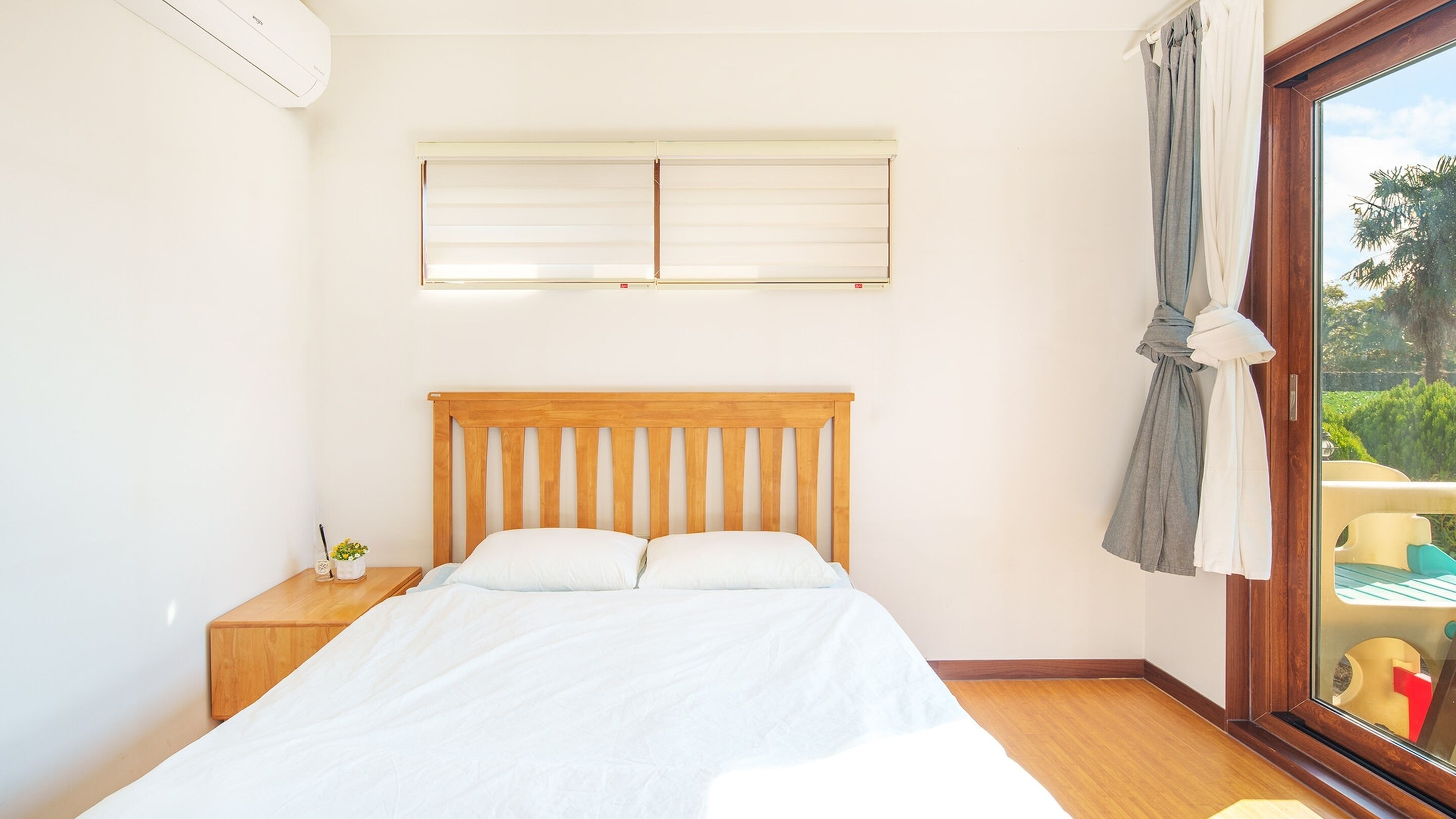 A bedroom with a wooden bed, a nightstand, a window with curtains, and a ceiling fan.