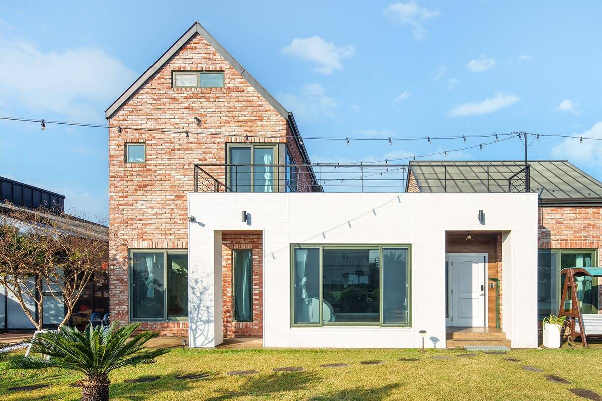 A modern two-story house with a brick facade, large windows, and a small front porch.