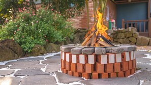 A fire pit with a brick base and a metal rim, surrounded by a stone pathway. - Jeju Brickninemansion (Jeju City)