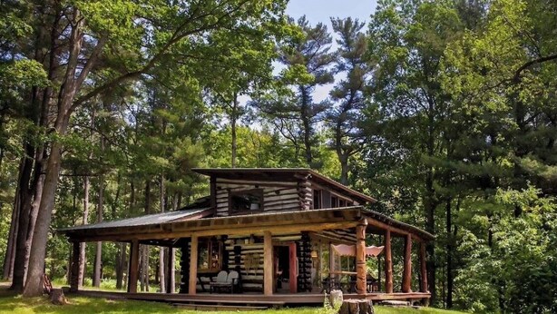 Eine rustikale Holzhütte mit Veranda, umgeben von dichtem Wald.