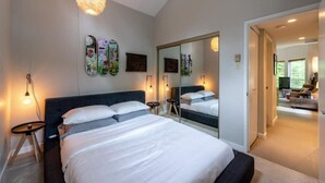 A bedroom with a large bed, bedside tables, a mirror, and a hanging light fixture. - Lux Townhome in the Trees - Walk to lifts! (Whistler)