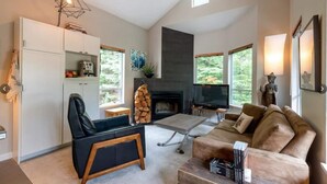 A modern living room with a fireplace, a sofa, a coffee table, and a TV. - Lux Townhome in the Trees - Walk to lifts! (Whistler)