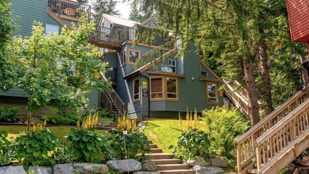 A multi-story house with a staircase leading to a deck, surrounded by lush greenery and trees. - Lux Townhome in the Trees - Walk to lifts! (Whistler)