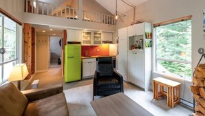 A modern apartment with a loft bedroom, a kitchen with white cabinets, a green refrigerator, and a large window offering a forest view. - Lux Townhome in the Trees - Walk to lifts! (Whistler)