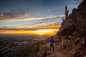 Eine Person steht auf einem Felsen und blickt auf eine Stadt bei Sonnenuntergang.