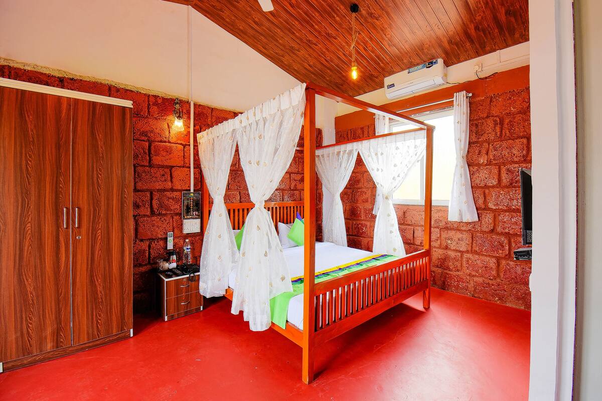A four-poster bed with white curtains, a wooden wardrobe, and a brick wall.
