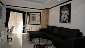 A modern living room with a black leather sofa, a glass coffee table, a white desk with a chair, and a ceiling fan.