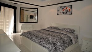 A bedroom with a large bed, a mirror, a painting, and a white dresser.