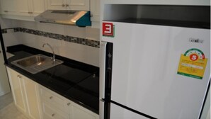 A kitchen with white cabinets, a black countertop, a stainless steel sink, and a white refrigerator with a sticker.