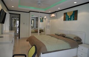 Relax in this serene bedroom with a comfortable bed, bedside table, and chair, featuring a mounted TV and a beautiful painting above the bed.