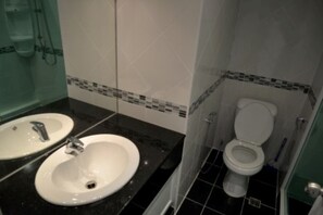 Bathroom features two sinks and a toilet, with a shower area and glass partition.
