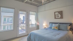 Un dormitorio con cama, dos ventanas, un mapa de Georgia colgado en la pared y un balcón con vistas a edificios.