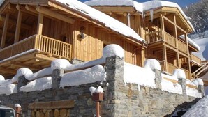 A wooden chalet with balconies covered in snow, stone walls, and a wooden staircase leading up to the entrance. - Sainte Foy Self-Catered Ski Apartment (Sainte Foy Tarentaise Station)