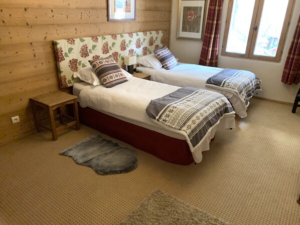 Una habitación acogedora con dos camas, una mesita de noche de madera, una alfombra y una ventana con cortinas.
