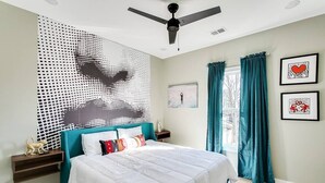A bedroom with a bed, a ceiling fan, a wall art piece, and curtains.