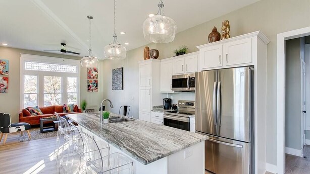 A modern kitchen with a large island, stainless steel appliances, and pendant lighting.