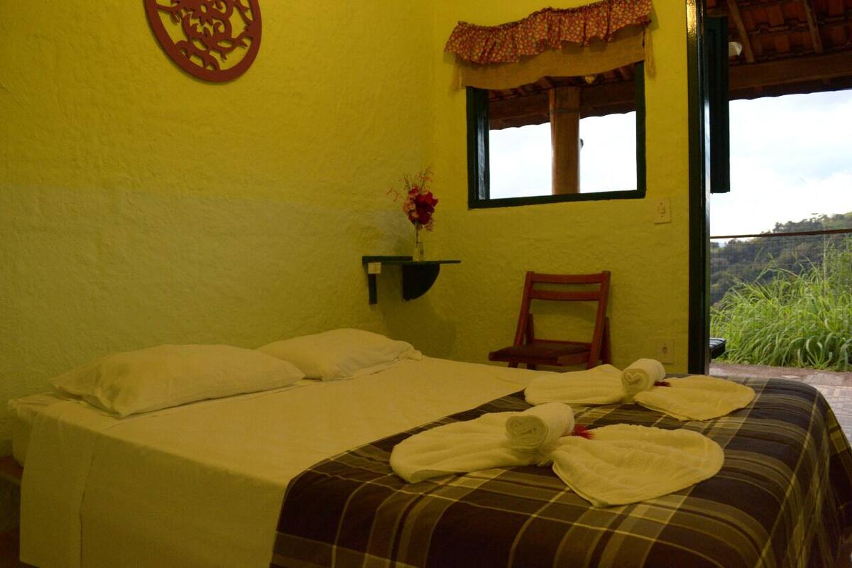 A room with a bed, a chair, a window, and a wall decoration.