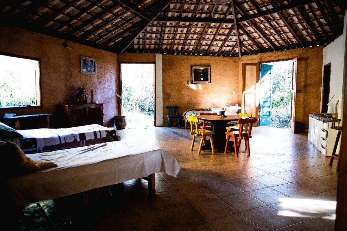 A room with a bed, a table, chairs, and a kitchen area.