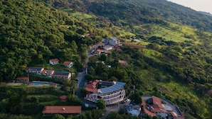 An aerial view of a hillside village with houses, a winding road, and a prominent building with a curved roof. - Pousada Saúde Melhor (Extrema)