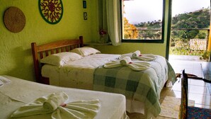 A hotel room with two beds, a wooden headboard, a window with a view of a hillside, and a small table with a chair. - Pousada Saúde Melhor (Extrema)