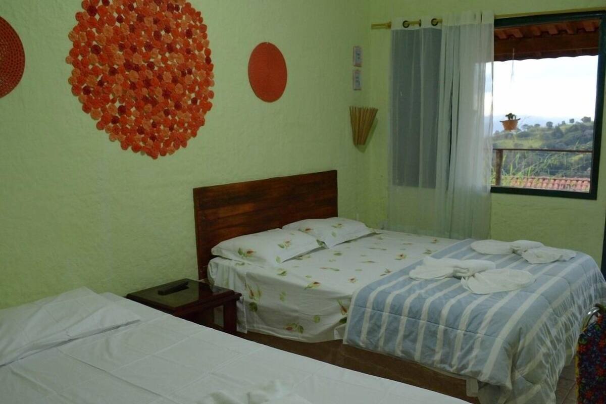 A room with two beds, a wooden headboard, a nightstand, and a window with curtains.