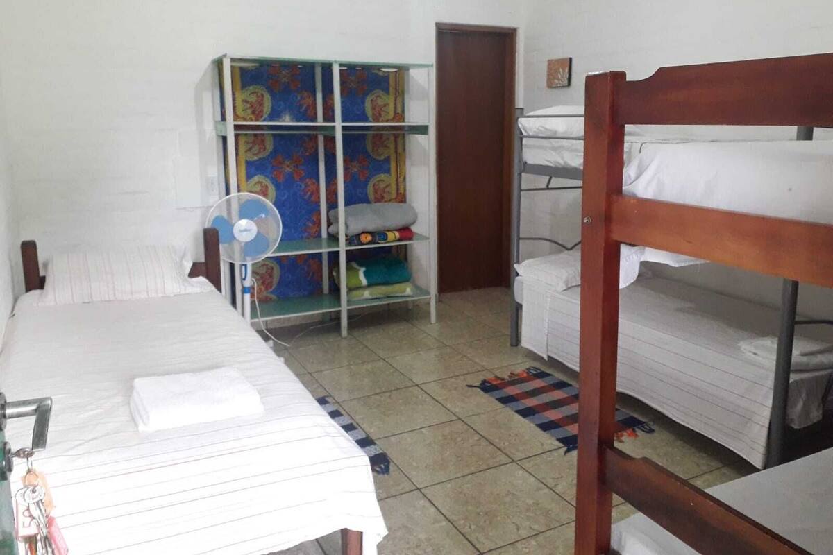 A dormitory room with bunk beds, a fan, a wardrobe, and a tiled floor.