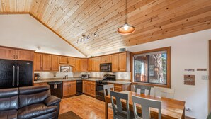 A modern kitchen with wooden cabinets, a black refrigerator, a microwave, and a dining area with a wooden table and chairs. - Clean & Cozy. Walk to 3 beaches. Dog friendly. (Tahoe City)