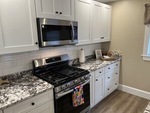 A modern kitchen with white cabinets, a stainless steel microwave, a gas stove, and a built-in oven. - Newly renovated 3 bedroom, 2 bath bungalow, just steps to downtown BBH. (Boothbay Harbor)