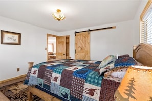 Ein Schlafzimmer mit einem hölzernen Bett, einer Steppdecke, einer Holztür und einer Deckenleuchte.