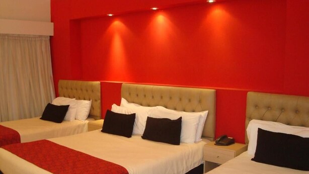 A hotel room with three beds, each with a red and white bedspread, and a red accent wall. - Vidda y Viken Apart Hotel (Mar del Plata)