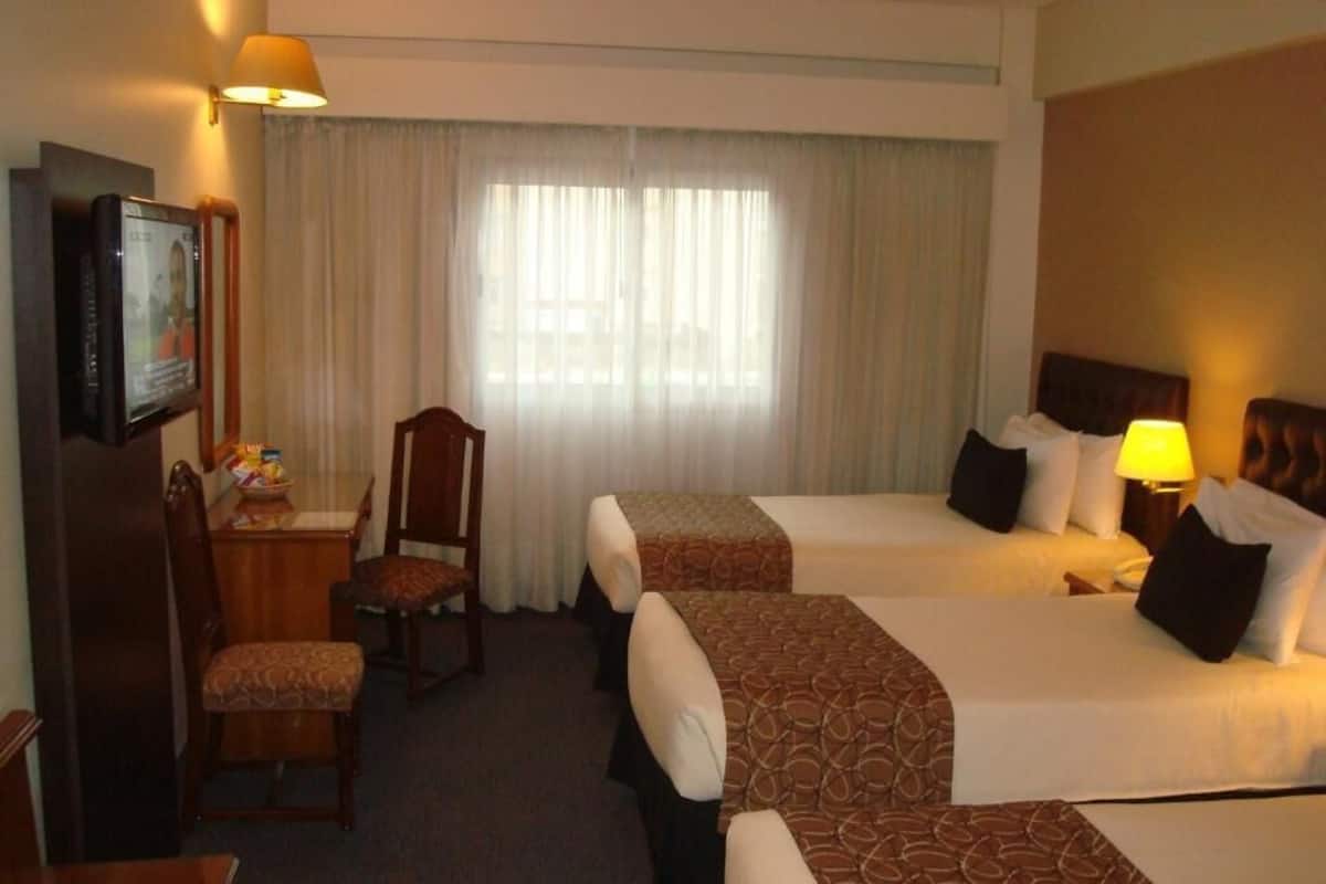 Una camera d'albergo con due letti, una scrivania, una sedia e una televisione.