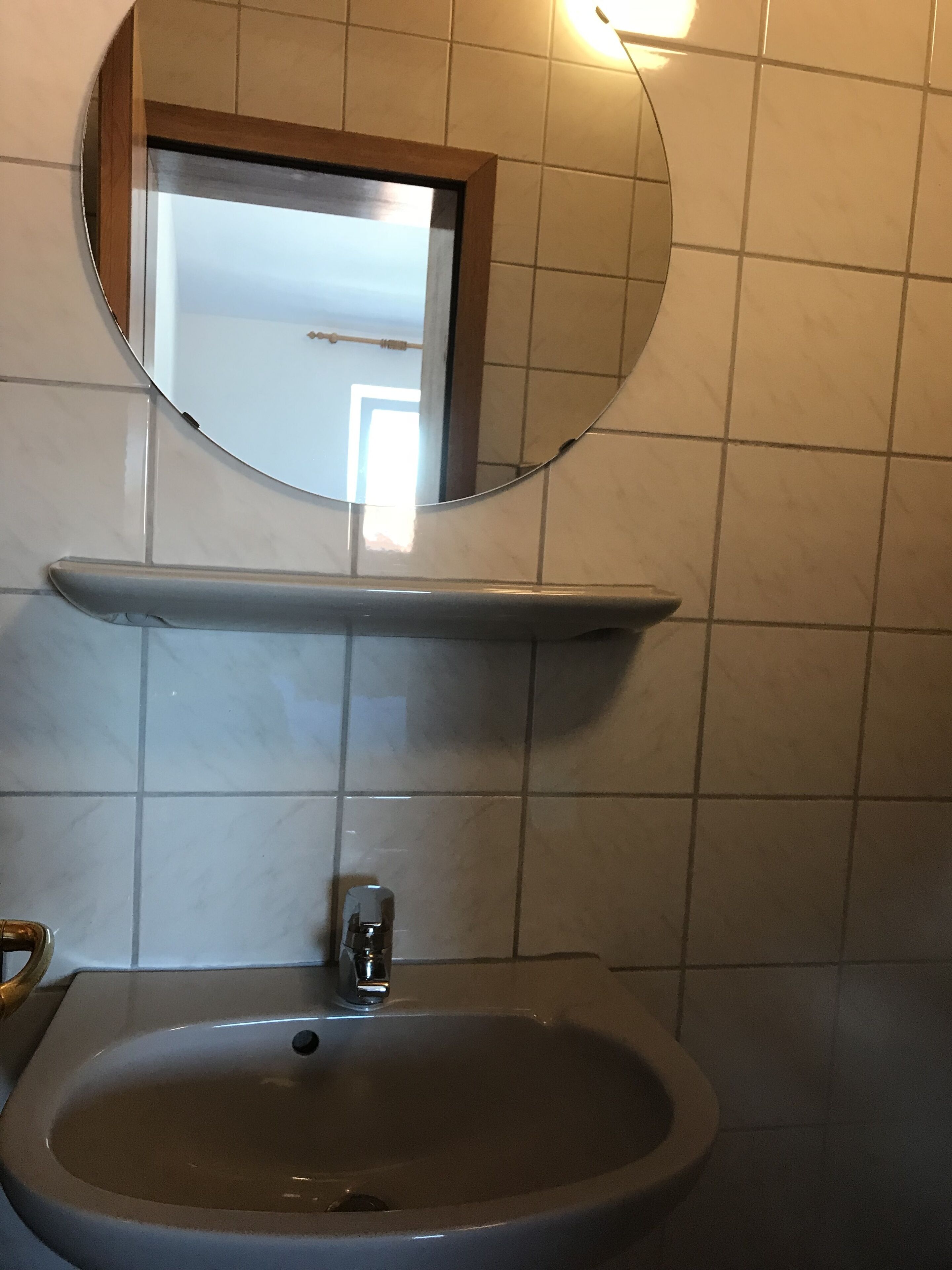 Un baño con un espejo redondo, un lavamanos y un inodoro.