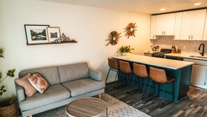 A modern kitchen with white cabinets, a central island with bar stools, a grey sofa, and a round wooden coffee table. - Riverfront Condo 2 blocks to downtown Bend (Bend)