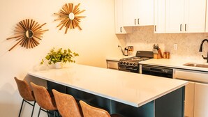 A modern kitchen with a central island, four bar stools, a stove, and white cabinets. - Riverfront Condo 2 blocks to downtown Bend (Bend)