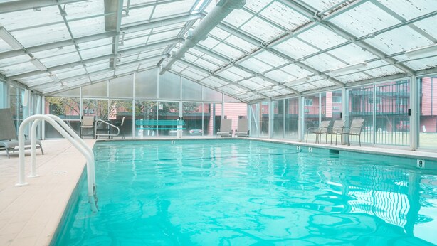 An indoor swimming pool with clear glass walls, a pool ladder, and lounge chairs. - Riverfront Condo 2 blocks to downtown Bend (Bend)