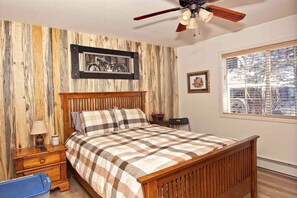 A bedroom with a wooden bed, a nightstand, a lamp, a ceiling fan, and a window with blinds.
