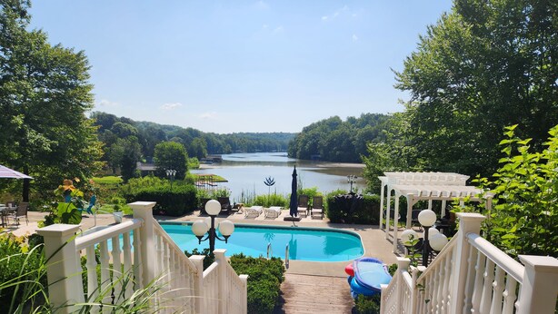 A pool area with a view of a lake, surrounded by greenery and a gazebo. - Blackwater Castle w/ Private Pool, Arcade, Hot Tub (Wirtz)