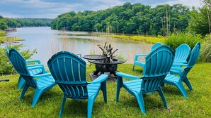 A lakeside outdoor seating area with four blue Adirondack chairs and a round table with a fire pit. - Blackwater Castle w/ Private Pool, Arcade, Hot Tub (Wirtz)