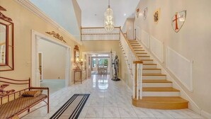 A spacious hallway with a marble floor, a wooden staircase, and a chandelier. - Blackwater Castle w/ Private Pool, Arcade, Hot Tub (Wirtz)