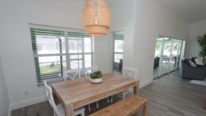 A dining area with a wooden table and benches, white chairs, and a hanging light fixture. - Discover the perfect vacation rental 3BRD, 2 Bath, heated pool, lanai, parking (Cape Coral)