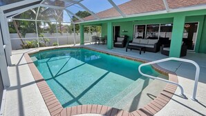 A pool area with a glass enclosure, a patio with outdoor furniture, and a view of the surrounding landscape. - Discover the perfect vacation rental 3BRD, 2 Bath, heated pool, lanai, parking (Cape Coral)