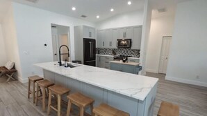 A modern kitchen with a marble island, wooden stools, and light-colored cabinetry. - Discover the perfect vacation rental 3BRD, 2 Bath, heated pool, lanai, parking (Cape Coral)