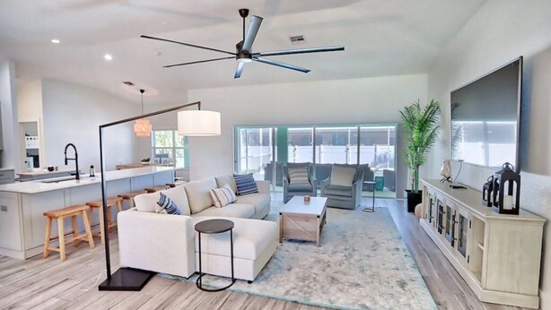 A spacious living area with a ceiling fan, a sofa, a coffee table, and a TV on a cabinet. - Discover the perfect vacation rental 3BRD, 2 Bath, heated pool, lanai, parking (Cape Coral)