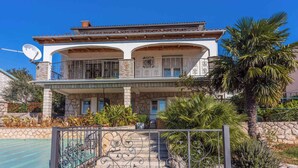 Ein zweistöckiges Haus mit Balkon, Steinhausfassade und einem Swimmingpool im Hintergrund.